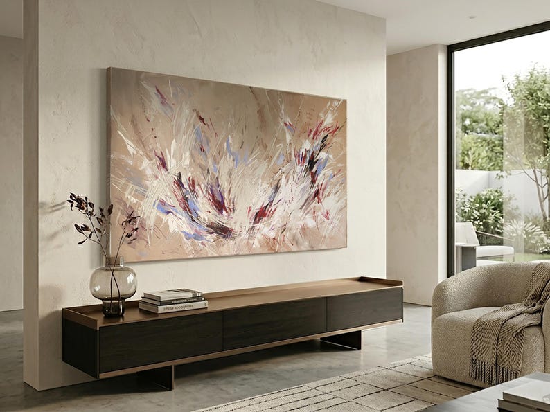 May include: Large abstract painting with beige, white, red, and blue brushstrokes. The artwork hangs above a dark wood and metal console table. A glass vase with decorative branches sits on the table, alongside books. A modern living room setting.