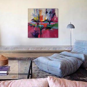 May include: An abstract painting with vibrant colors of red, pink, yellow, and blue hangs on a white wall. A gray floor lamp and a light blue lounge chair with a matching ottoman are in the room. A glass coffee table and a decorative wooden box are also visible.