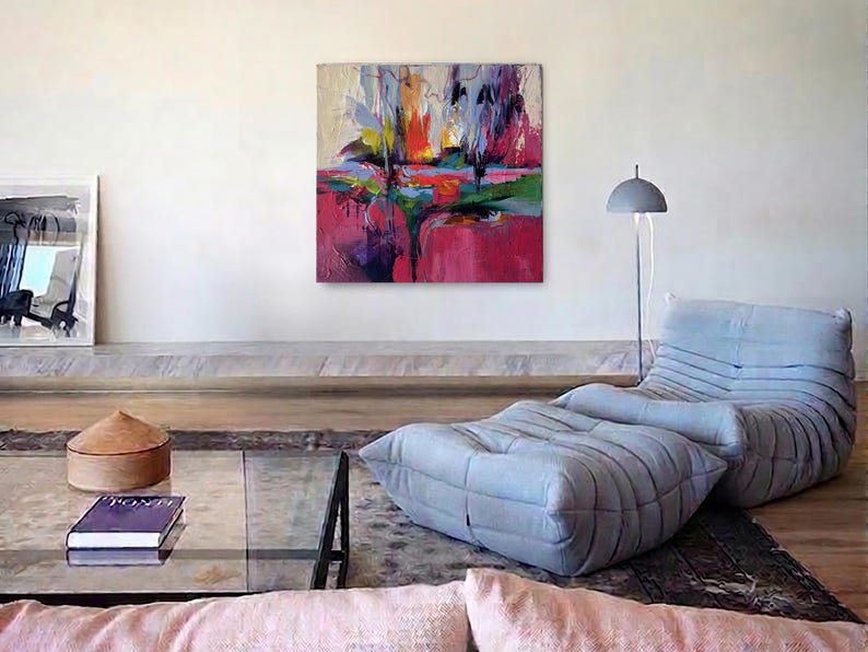 May include: An abstract painting with vibrant colors of red, pink, yellow, and blue hangs on a white wall. A gray floor lamp and a light blue lounge chair with a matching ottoman are in the room. A glass coffee table and a decorative wooden box are also visible.