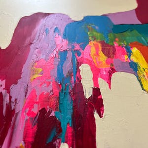 May include: Abstract artwork with bold brushstrokes in a variety of colours. The painting showcases pink, red, blue, yellow, and green shades, set against a creamy off-white backdrop. The textured paint application gives a dynamic and expressive feel.