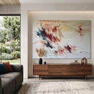 May include: A modern living room featuring a large abstract painting with red, blue, and yellow brushstrokes. Below the artwork is a wooden cabinet with three doors, and a gray sofa with colorful throw pillows. A patterned rug and large windows complete the scene.