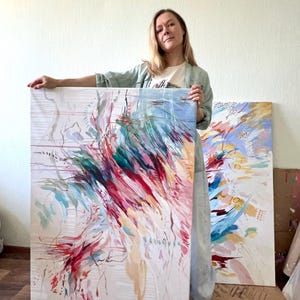May include: Two abstract paintings with vibrant brushstrokes in red, teal, pink, and blue hues. The artwork is on a white canvas, with a light beige background. The paintings are displayed in a well-lit room.