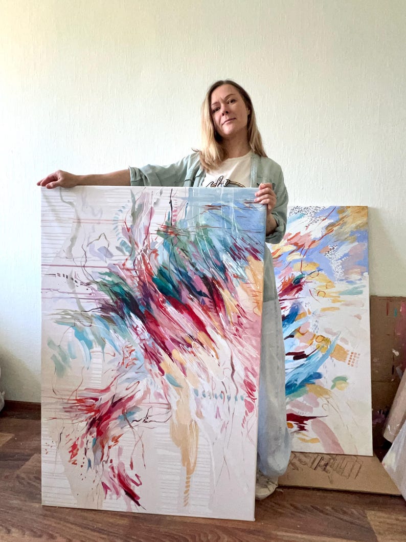 May include: Two abstract paintings with vibrant brushstrokes in red, teal, pink, and blue hues. The artwork is on a white canvas, with a light beige background. The paintings are displayed in a well-lit room.