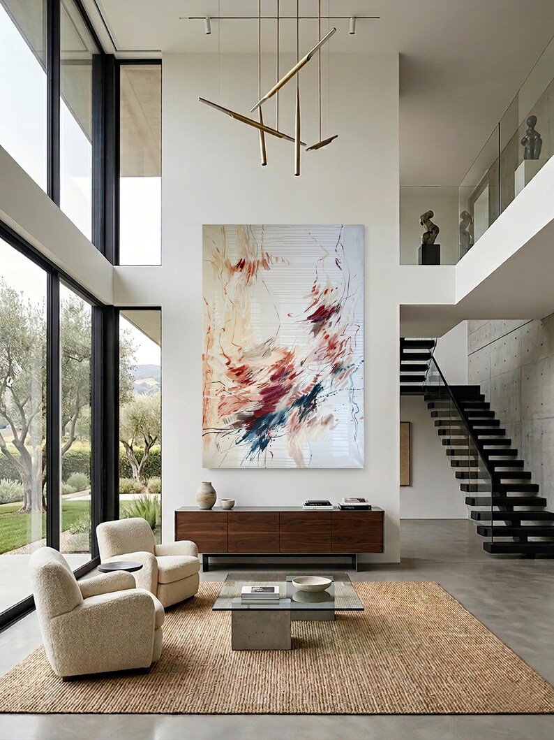 May include: Modern living room with large windows, a neutral color palette, and an abstract painting. Two cream-colored armchairs face a glass coffee table and a wooden cabinet. A woven rug covers the floor.