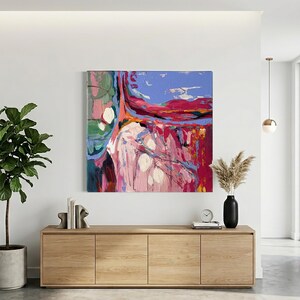 May include: Abstract painting with a vibrant color palette of pink, red, blue, and green. The artwork is displayed on a white wall above a wooden cabinet. A potted plant and decorative items complete the interior design.