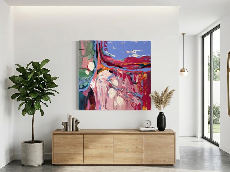 May include: Abstract painting with a vibrant color palette of pink, red, blue, and green. The artwork is displayed on a white wall above a wooden cabinet. A potted plant and decorative items complete the interior design.