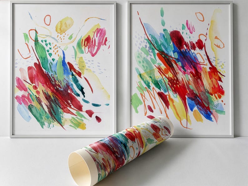 May include: Two framed rectangular wall art prints featuring abstract watercolor brushstrokes in vibrant red, blue, green, and yellow hues. A rolled paper print with matching colorful abstract patterns is positioned in the foreground.