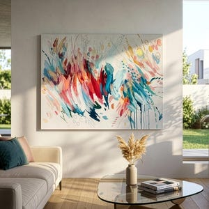 Pode incluir: Uma grande pintura retangular em tela com uma composi&ccedil;&atilde;o abstrata de pinceladas energ&eacute;ticas em tons de vermelho, azul-petr&oacute;leo, laranja e amarelo sobre um fundo branco, exibida numa parede acima de um sof&aacute; e uma mesa de centro.