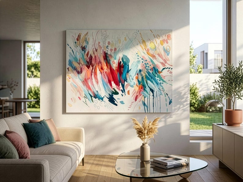 Pode incluir: Uma grande pintura retangular em tela com uma composi&ccedil;&atilde;o abstrata de pinceladas energ&eacute;ticas em tons de vermelho, azul-petr&oacute;leo, laranja e amarelo sobre um fundo branco, exibida numa parede acima de um sof&aacute; e uma mesa de centro.