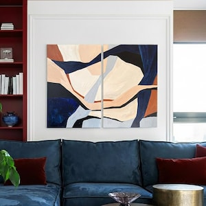 May include: Abstract art diptych with a modern design. The artwork features a combination of shapes and colors, including navy blue, beige, and rust. The painting is displayed above a blue sectional sofa with burgundy throw pillows.