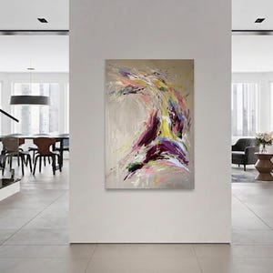 May include: Abstract painting with a dynamic composition of swirling brushstrokes. The artwork features a palette of purple, yellow, pink, and green against a neutral background. The painting is displayed in a modern, minimalist interior.