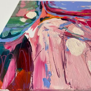 May include: Abstract painting with a palette of pink, teal, and orange. The artwork features thick brushstrokes and textured paint, with white and purple accents. The canvas is viewed from a side angle, showcasing the edges and depth of the piece.