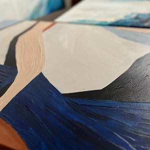 May include: Close-up of an abstract painting with textured brushstrokes. The artwork features a palette of navy blue, beige, black, and white. The composition is geometric, with shapes and lines creating a modern aesthetic. The painting is on a canvas.