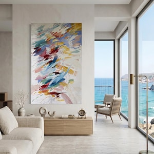 Puede incluir: Pintura abstracta con pinceladas coloridas en rojo, azul, amarillo y rosa sobre fondo blanco. La obra de arte cuelga en un sal&oacute;n moderno con vistas al mar.