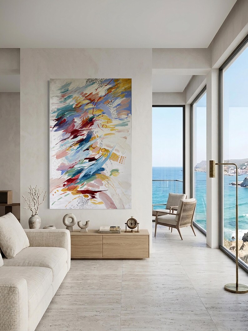 Puede incluir: Pintura abstracta con pinceladas coloridas en rojo, azul, amarillo y rosa sobre fondo blanco. La obra de arte cuelga en un sal&oacute;n moderno con vistas al mar.