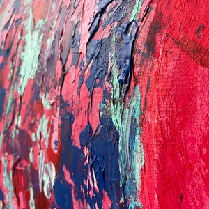 May include: Close-up of an abstract painting with thick brushstrokes. The artwork features a vibrant palette of red, blue, pink, and green hues. The textured surface of the canvas is visible, showcasing the artist's technique and the depth of the colors.