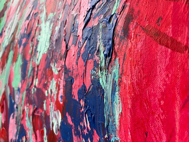 May include: Close-up of an abstract painting with thick brushstrokes. The artwork features a vibrant palette of red, blue, pink, and green hues. The textured surface of the canvas is visible, showcasing the artist's technique and the depth of the colors.