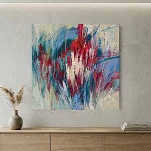 May include: Abstract painting with a vibrant display of colors. The artwork features bold brushstrokes in shades of red, blue, and white, creating a dynamic and textured composition. The painting is mounted on a neutral-toned wall above a wooden cabinet.