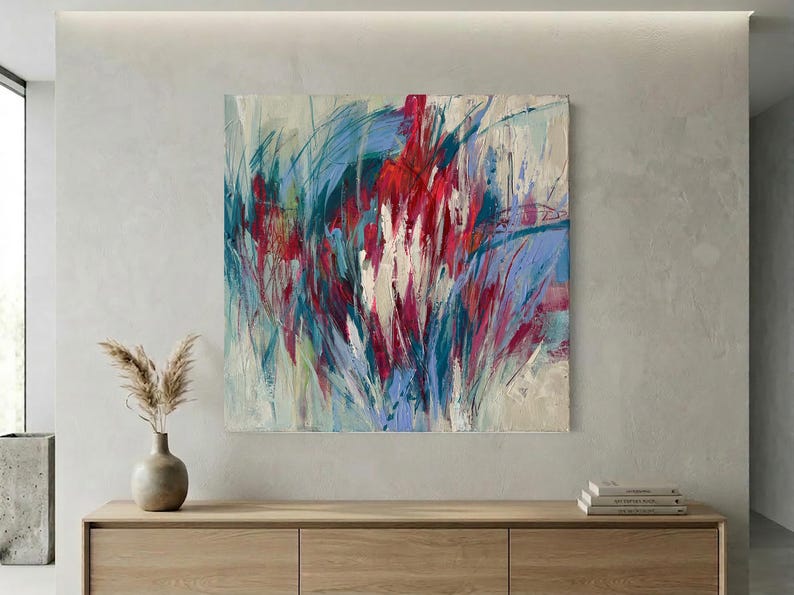 May include: Abstract painting with a vibrant display of colors. The artwork features bold brushstrokes in shades of red, blue, and white, creating a dynamic and textured composition. The painting is mounted on a neutral-toned wall above a wooden cabinet.