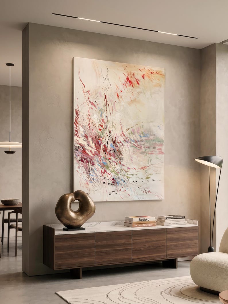 May include: A large vertical abstract painting with red, pink, and green brushstrokes on a cream background, displayed above a dark wood sideboard with a bronze sculptural object and two books, one titled Rothko, resting on the white marble top.