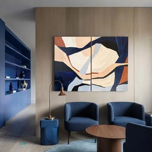 May include: An interior design scene featuring a modern living room with blue furniture and abstract art. The room includes a blue built-in shelving unit, two blue armchairs, and a round wooden coffee table. The artwork is a two-panel abstract painting with beige, blue, and brown shapes.