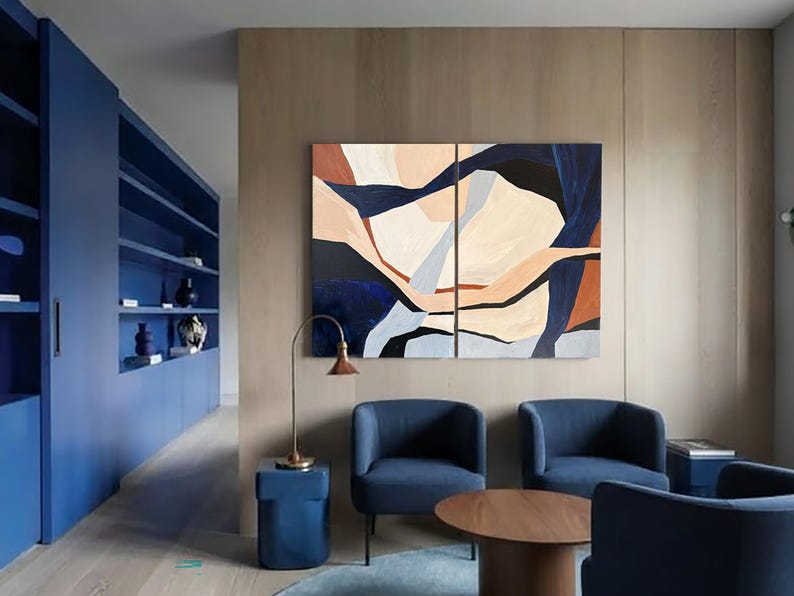 May include: An interior design scene featuring a modern living room with blue furniture and abstract art. The room includes a blue built-in shelving unit, two blue armchairs, and a round wooden coffee table. The artwork is a two-panel abstract painting with beige, blue, and brown shapes.