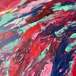 May include: Close-up of an abstract painting with thick brushstrokes. The artwork features a vibrant mix of colors, including shades of red, pink, blue, and green. The textured surface creates a dynamic and expressive visual effect, suggesting a modern art style.