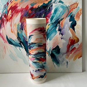 K&ouml;nnte beinhalten: Ein zylindrischer Papierdruck mit einem lebendigen abstrakten Gem&auml;lde, das kr&auml;ftige, ausdrucksstarke Pinselstriche in T&uuml;rkis, Dunkelblau, Magenta, Orange und Creme zeigt. Der Druck steht aufrecht vor einer passenden gro&szlig;en quadratischen Leinwand.