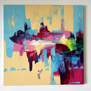 May include: Abstract painting with a square canvas. The artwork features a blend of colors, including light blue, yellow, pink, red, purple, and green. The brushstrokes are visible, creating a textured effect. The painting is mounted on a white wall.