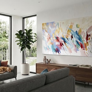 Puede incluir: Un sal&oacute;n moderno con una gran pintura abstracta con vibrantes pinceladas en rojo, azul, amarillo y blanco. Un mueble de madera oscura alberga objetos decorativos y libros. Un sof&aacute; gris con cojines azules y naranjas y un gato naranja durmiendo.