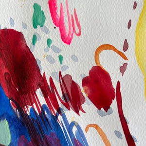 May include: An abstract watercolor painting on textured white paper featuring bold splashes of deep red, vibrant blue, bright yellow, and hot pink. The composition includes thin orange curved lines, small grey dashes, and green paint spots.