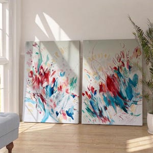 Op de afbeelding: Twee rechthoekige schilderijen op canvas met abstracte composities met levendige spatten van rode, blauwgroene en zachtroze verfstreken tegen een lichtgrijze achtergrond. Het kunstwerk toont dynamische, energieke penseelstreken en gelaagde kleurmarkeringen.