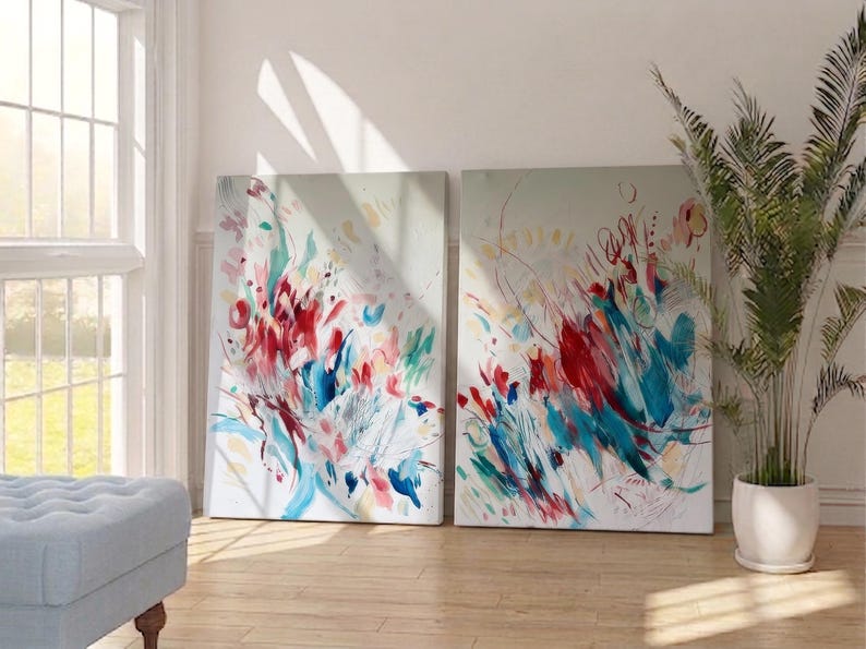 Op de afbeelding: Twee rechthoekige schilderijen op canvas met abstracte composities met levendige spatten van rode, blauwgroene en zachtroze verfstreken tegen een lichtgrijze achtergrond. Het kunstwerk toont dynamische, energieke penseelstreken en gelaagde kleurmarkeringen.