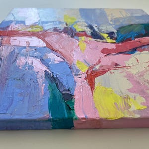 May include: An abstract painting on canvas with bold brushstrokes. The artwork uses pink, blue, yellow, and red colours. The texture of the paint is visible, creating a dynamic surface. The painting is mounted on a square canvas.