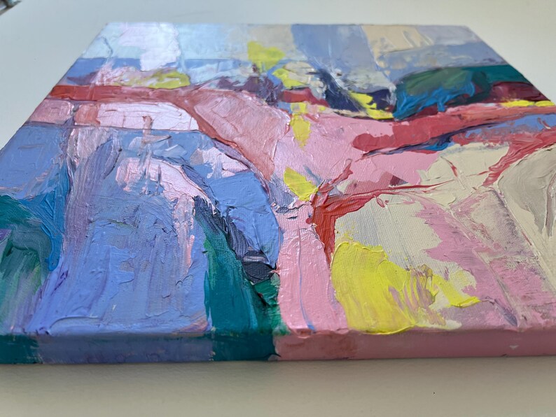 May include: An abstract painting on canvas with bold brushstrokes. The artwork uses pink, blue, yellow, and red colours. The texture of the paint is visible, creating a dynamic surface. The painting is mounted on a square canvas.