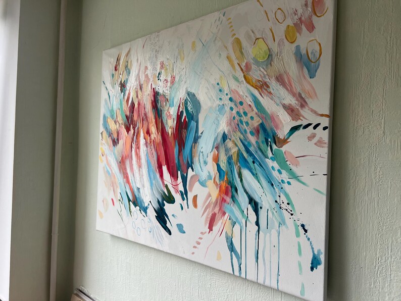 Pode incluir: Uma pintura retangular em tela com uma composi&ccedil;&atilde;o abstrata de pinceladas energ&eacute;ticas em tons de azul-petr&oacute;leo, rosa brilhante, vermelho profundo e amarelo sobre fundo branco, acentuada por pequenos pontos, c&iacute;rculos e gotas de tinta.
