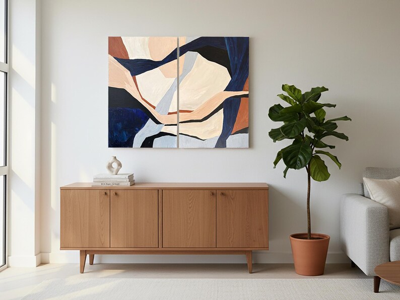 May include: Abstract art piece in a living room setting. The artwork is split into two panels, featuring a design with navy, beige, and rust tones. A wooden cabinet with four doors sits below the art. A potted plant and a sofa complete the scene.