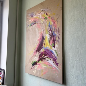 May include: Abstract painting on a large canvas. The artwork features a dynamic composition of colorful brushstrokes in shades of pink, purple, yellow, and blue against a neutral background. The painting is mounted on a wooden frame and displayed on a wall.