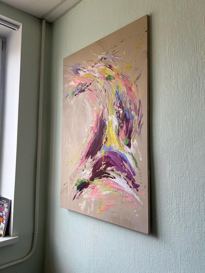May include: Abstract painting on a large canvas. The artwork features a dynamic composition of colorful brushstrokes in shades of pink, purple, yellow, and blue against a neutral background. The painting is mounted on a wooden frame and displayed on a wall.