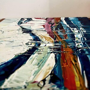 May include: Abstract painting with thick brushstrokes in shades of white, blue, orange, and pink. The artwork has a textured surface, creating a dynamic and expressive visual effect. The painting is on a square canvas.