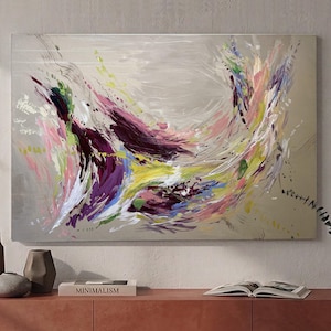 May include: Abstract painting with a neutral background and dynamic brushstrokes in shades of purple, pink, yellow, and green. The artwork features a burst of color and movement, creating a vibrant and energetic composition. The painting is displayed above a wooden cabinet with decorative vases and a book.