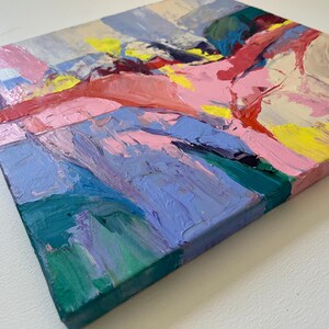 May include: Square abstract painting with thick brushstrokes in shades of pink, blue, yellow, and green. The artwork has a textured appearance, with visible paint layers creating a dynamic and colourful composition. The edges of the canvas are painted pink.
