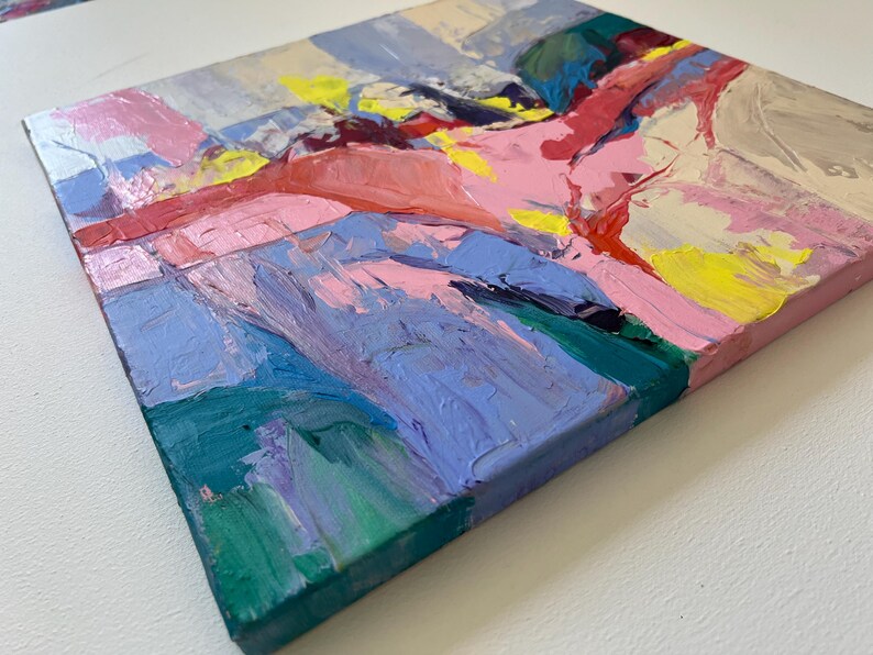 May include: Square abstract painting with thick brushstrokes in shades of pink, blue, yellow, and green. The artwork has a textured appearance, with visible paint layers creating a dynamic and colourful composition. The edges of the canvas are painted pink.