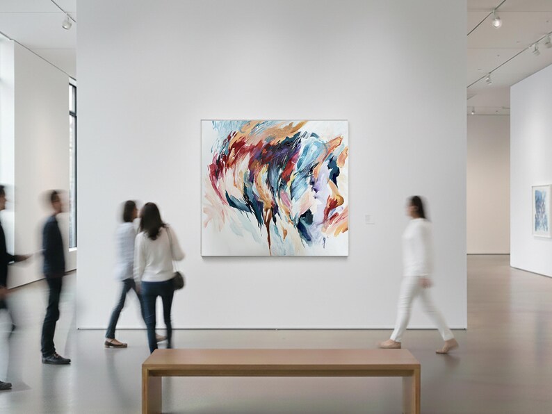 May include: An abstract painting with a mix of colors, including blue, red, and orange, hangs on a white wall in an art gallery. The artwork is the focal point, with blurred figures of people in the background.