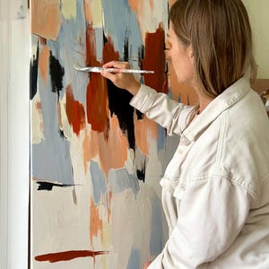 May include: A large rectangular canvas featuring an abstract painting with vertical brushstrokes in shades of terracotta, light blue, cream, and black. The composition displays layered paint textures and bold colour blocks applied across the surface.