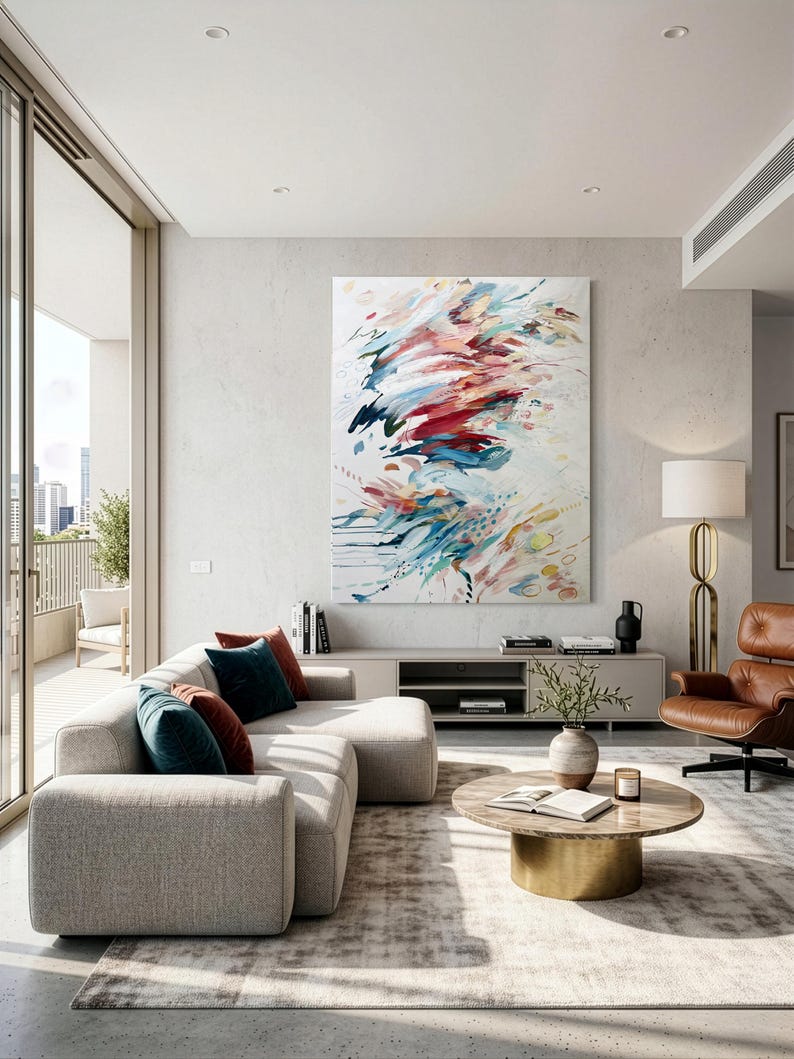 Pode incluir: Uma grande pintura retangular em tela com pinceladas abstratas em tons de vermelho, azul, azul-petr&oacute;leo e dourado sobre um fundo branco, exibida numa parede clara acima de um m&oacute;vel baixo numa sala de estar.
