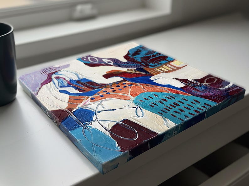 以下が含まれることがあります： 正方形の抽象絵画で、テクスチャ加工された表面です。この作品は、白、青、オレンジ、紫など、さまざまな色が混ざっています。構成はさまざまな形とパターンで構成されており、筆致が見え、塗料が厚く塗られています。