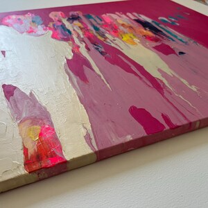 May include: Abstract painting on canvas with a vibrant color palette. The artwork features a combination of pink, white, yellow, and blue hues, with paint drips and textured brushstrokes. The canvas is stretched and mounted on a wooden frame.