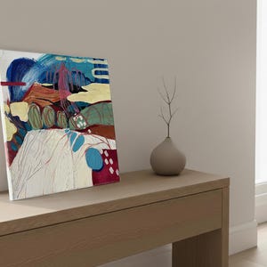 May include: Abstract art canvas with a mix of colors including blue, red, yellow, and green. The artwork features brushstrokes and shapes, creating a modern aesthetic. A small, gray vase with a twig is next to the canvas.