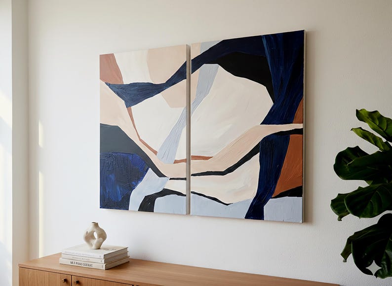 May include: Two abstract paintings with a modern design. The artwork features geometric shapes in shades of navy blue, beige, brown, and white. The paintings are mounted on a white wall above a wooden cabinet.